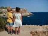 two children standing near cliff watching on ocean at daytime